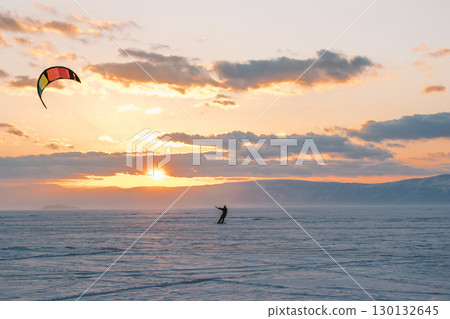 kite surfer maneuvers skillfully across vast winter landscape under vibrant sunset sky. 130132645