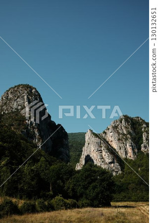 Majestic rocky peaks rising above dense green forest under a clear blue sky in Stara Planina, Serbia Majestic rocky peaks rising above dense green forest under a clear blue sky in Stara Planina, Serbia 130132651