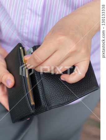 Close-up of a person opening a black leather wallet with a zipper. The individual is using both hands to access the wallet, revealing potential use for storing coins and cash. Close-up of a person opening a black leather wallet with a zipper. The individual is using both hands to access the wallet, revealing potential use for storing coins and cash. 130133338