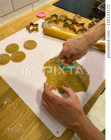 Person cutting stamped cookie dough on kitchen counter with cutters and rolling pin. 130133572