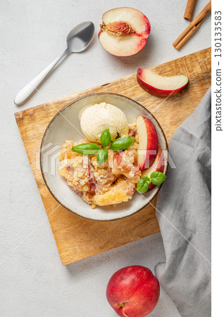 Peach crumble or cobbler with vanilla ice cream scoops and cinnamon in a plate on a wooden board 130133583
