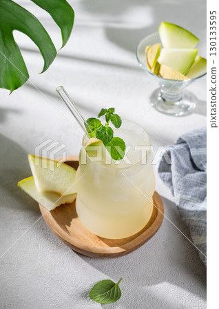 Refreshing lemonade or mojito in a glass with melon, straw and mint on a wooden plate  130133595