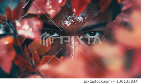 Person with a focused expression peers through colorful autumn leaves, capturing the essence of nature and emotion in a serene moment 130133934
