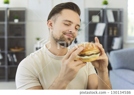 Young man enjoying delicious burger at home, close-up 130134586