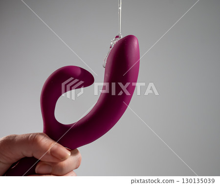 Lube pouring on pink dildo on white background.  130135039