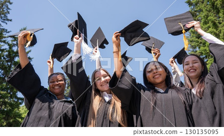 Young women of different nationalities pull graduation caps up.  130135095
