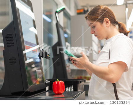 A woman buys bell peppers at a self-checkout.  130135254