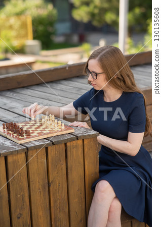 Caucasian woman playing chess outdoors. Caucasian woman playing chess outdoors. 130135608
