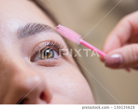 Caucasian woman brushing her eyelashes after lamination.  130135628
