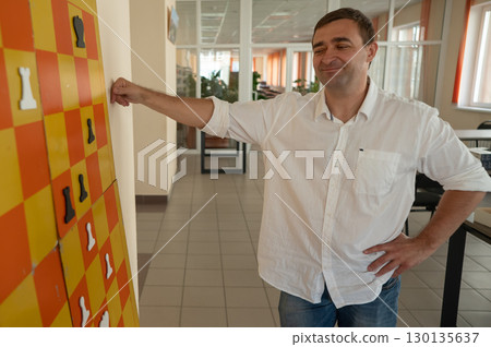 Caucasian man standing at wall mounted magnetic chessboard demonstration.  130135637