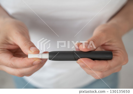 A woman inserts a cigarette stick into a tobacco heating system. Electronic cigarette. A woman inserts a cigarette stick into a tobacco heating system. Electronic cigarette. 130135650