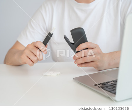 A woman takes a tobacco heating system out of a charger. Electronic cigarette. A woman takes a tobacco heating system out of a charger. Electronic cigarette. 130135656