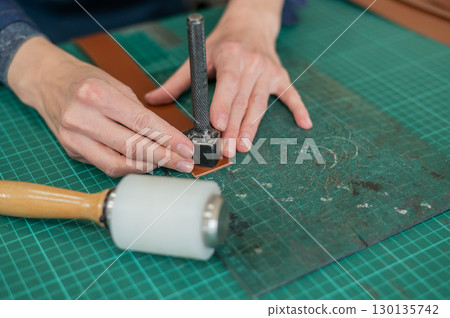 Woman tanner processes the edges of a leather belt in a workshop. Woman tanner processes the edges of a leather belt in a workshop. 130135742