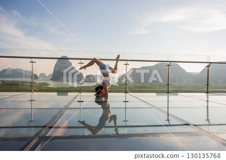 Caucasian woman doing forearm stand on glass bridge among mountains.  130135768