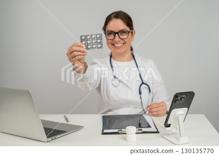 A female doctor sits at a table and recommends pills.  130135770