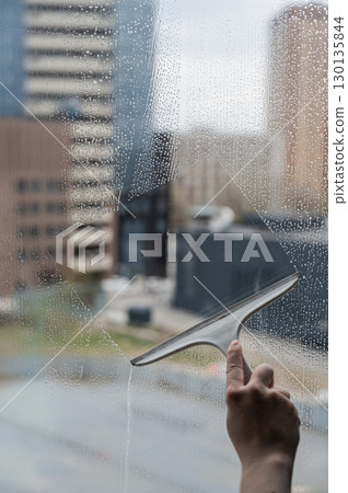 A woman washes a window with a scraper.  130135844
