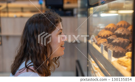 Caucasian woman looks greedily at baked goods in a bakery. Caucasian woman looks greedily at baked goods in a bakery. 130135854