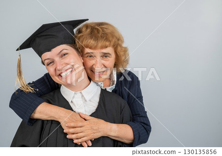 Portrait of Caucasian woman in graduation gown with her mother. Portrait of Caucasian woman in graduation gown with her mother. 130135856
