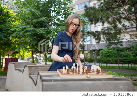Caucasian woman playing chess outdoors. Caucasian woman playing chess outdoors. 130135962
