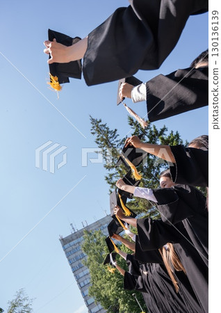 Young women of different nationalities pull graduation caps up.  130136139