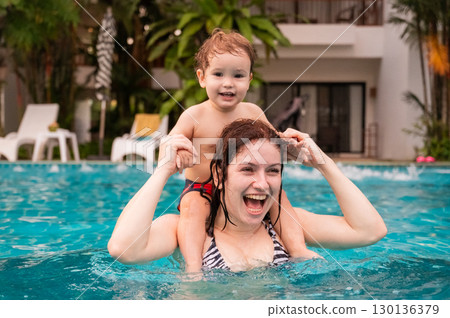 Caucasian woman holds her son while swimming in a pool on vacation. Mom teaches little boy to swim.  130136379
