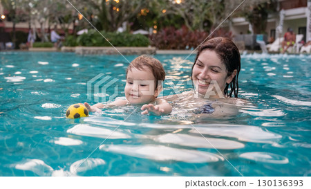 Caucasian woman holds son while swimming in pool on vacation. Caucasian woman holds son while swimming in pool on vacation. 130136393