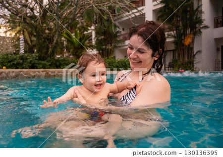 Caucasian woman holds her son while swimming in a pool on vacation. Mom teaches little boy to swim.  130136395