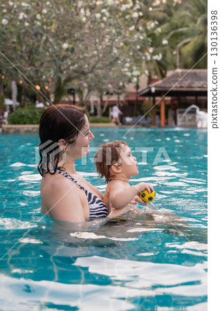 Caucasian woman holds her son while swimming in a pool on vacation. Mom teaches little boy to swim. Caucasian woman holds her son while swimming in a pool on vacation. Mom teaches little boy to swim. 130136398