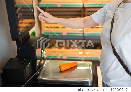 A woman weighs carrots at a self-checkout.  130136542