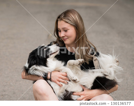 Young caucasian woman sitting on asphalt and hugging border collie dog.  130136577