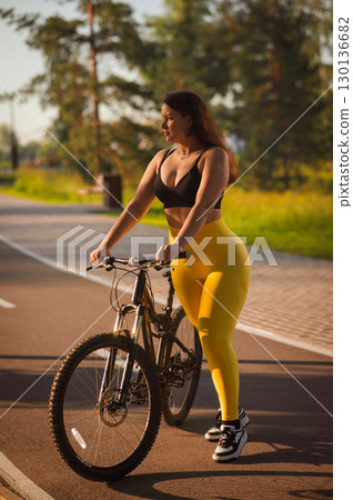 Curvy Caucasian Woman Riding Bicycle in Park. Curvy Caucasian Woman Riding Bicycle in Park. 130136682
