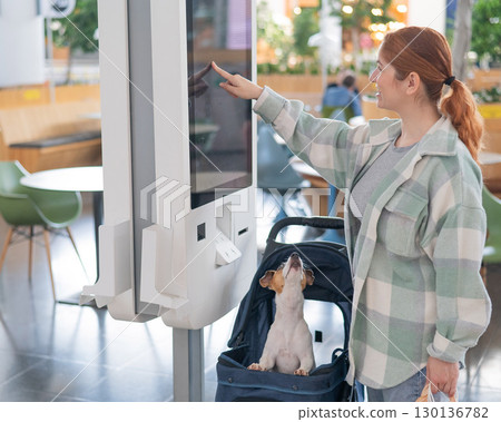 Caucasian woman makes a purchase at a self-service counter with a Jack Russell terrier dog in a stroller in a shopping center. Caucasian woman makes a purchase at a self-service counter with a Jack Russell terrier dog in a stroller in a shopping center. 130136782