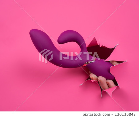 Female hand sticking out with raspberry sex toy from pink paper background. Female hand sticking out with raspberry sex toy from pink paper background. 130136842