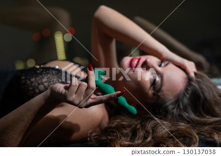 Woman in lace lingerie holding green anal beads.  130137038