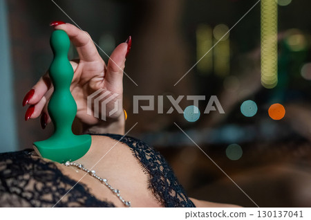 Woman in lace lingerie holding green anal beads. Woman in lace lingerie holding green anal beads. 130137041