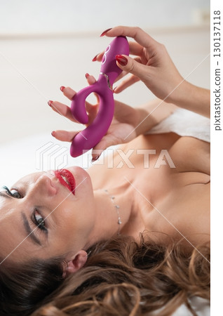 Caucasian woman in Santa Claus costume on bed holding curved sex toy. Caucasian woman in Santa Claus costume on bed holding curved sex toy. 130137118