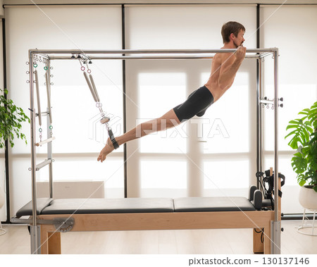 A man performs aerial exercises on a reformer machine. 130137146