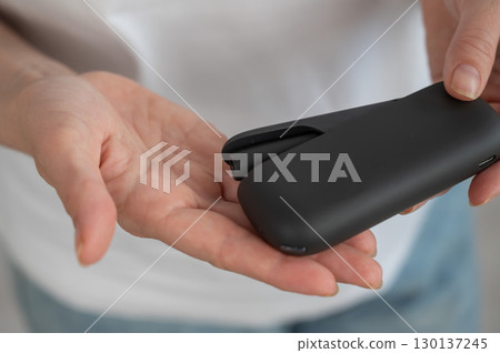 A woman takes a tobacco heating system out of a charger. Electronic cigarette. A woman takes a tobacco heating system out of a charger. Electronic cigarette. 130137245