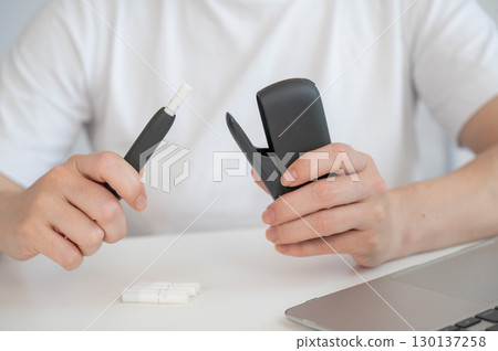A woman takes a tobacco heating system out of a charger. Electronic cigarette. 130137258