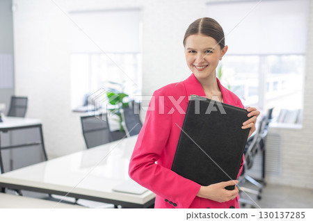 Smiling business woman in pink jacket holding folder with documents.  130137285