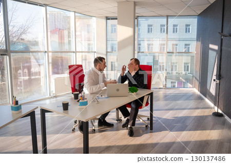 Two Caucasian men chatting in an office.  130137486