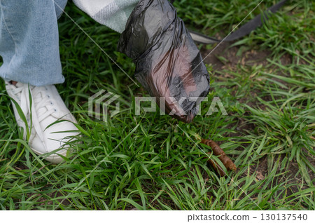 A woman cleans up dog excrement while on a walk. 130137540