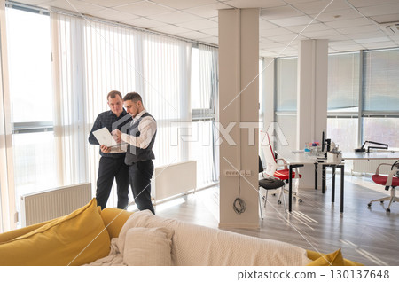 Two Caucasian men looking at a laptop and discussing work.  130137648