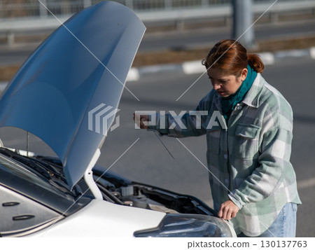 Caucasian female driver checking oil level in car engine. Caucasian female driver checking oil level in car engine. 130137763