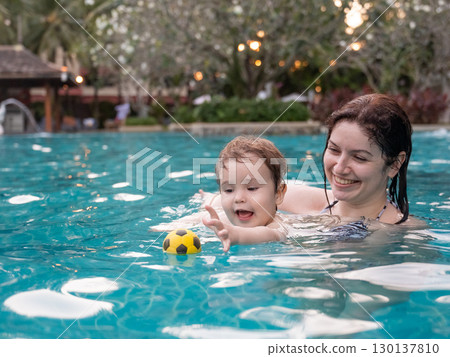 Caucasian woman holds her son while swimming in a pool on vacation. Mom teaches little boy to swim. Caucasian woman holds her son while swimming in a pool on vacation. Mom teaches little boy to swim. 130137810
