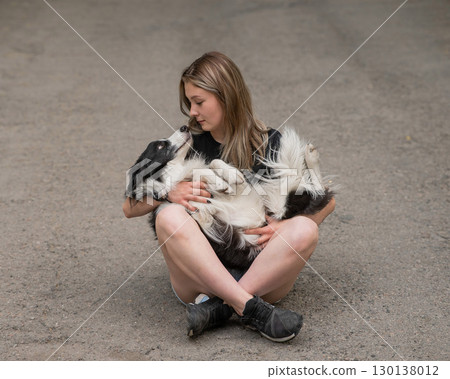 Young caucasian woman sitting on asphalt and hugging border collie dog.  130138012