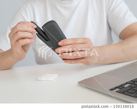 A woman takes a tobacco heating system out of a charger. Electronic cigarette. 130138018