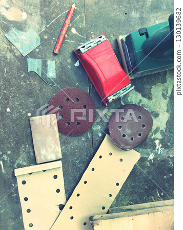 Vintage sander with abrasive discs and sandpaper sheets scattered across weathered workshop floor creating rustic craftsmanship atmosphere Vintage sander with abrasive discs and sandpaper sheets scattered across weathered workshop floor creating rustic craftsmanship atmosphere 130139682