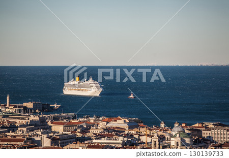 Luxury cruise ship anchored in deep blue Mediterranean waters near historic coastal Trieste city with terracotta rooftops 130139733