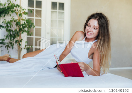 Woman in lingerie smiling and reading book in bedroom Woman in lingerie smiling and reading book in bedroom 130140192